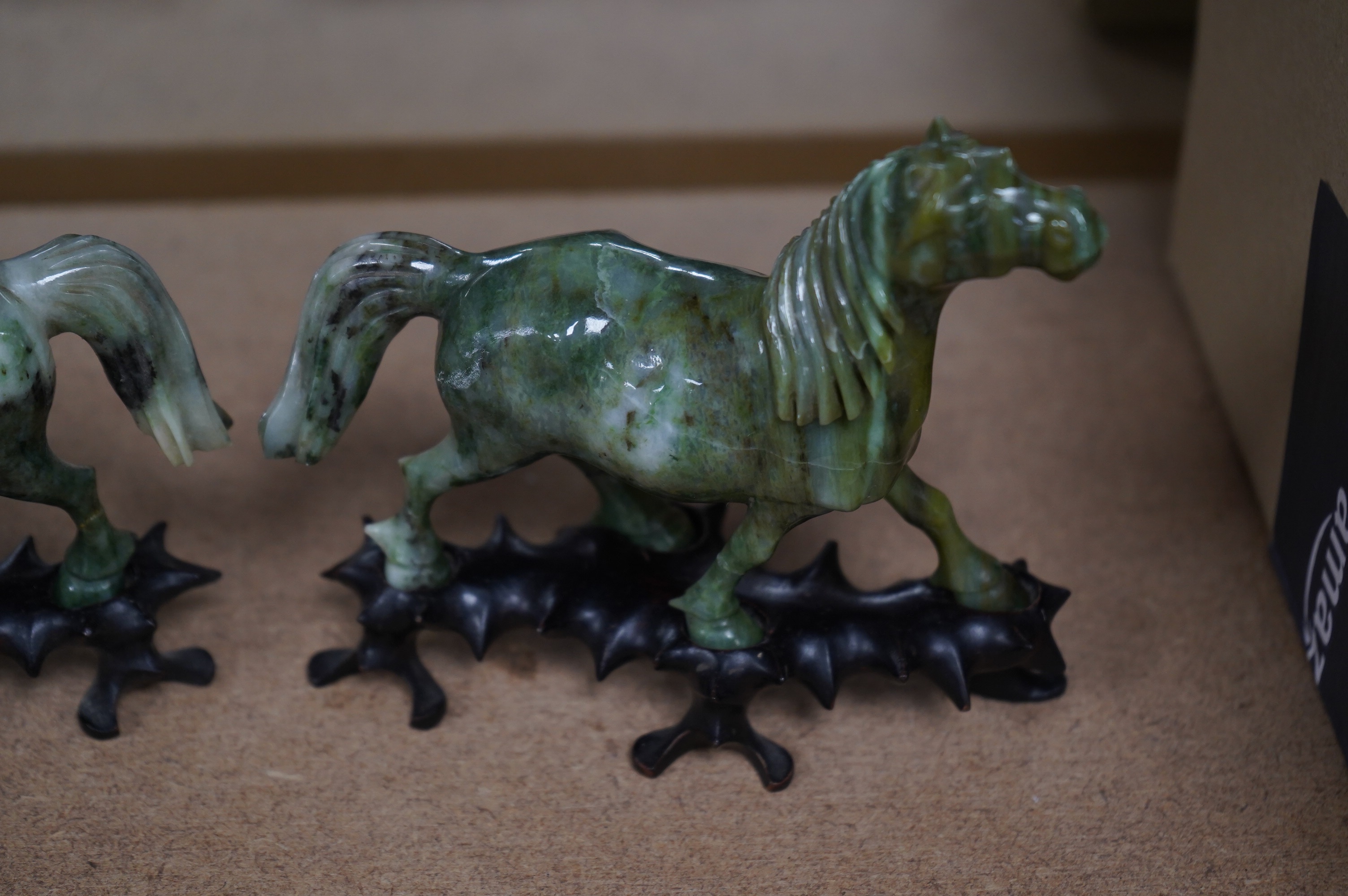 A pair of mid 20th century Chinese jadeite figures of horses, raised on hardwood stands, 13cm wide. Condition - fair, two legs broken and re-glued